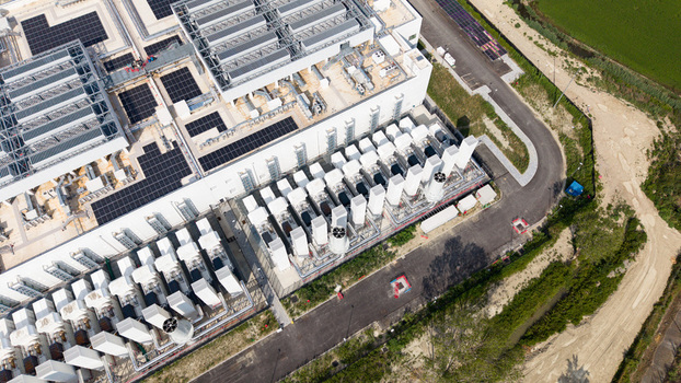 Aerial view of a modern data center campus featuring solar panels on the roof and industrial cooling units situated near a paved road in Melegnano Lombardy Italy.