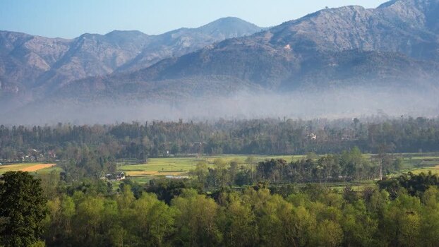View of lush green valley with misty Himalayas Nepal.