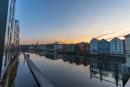 View of colorful historic wooden warehouses along the Nidelva river with reflections in the calm water at sunset Trondheim Trondelag Norway. View of colorful historic wooden warehouses along the Nidelva river with reflections in the calm water at sunset Trondheim Trondelag Norway.