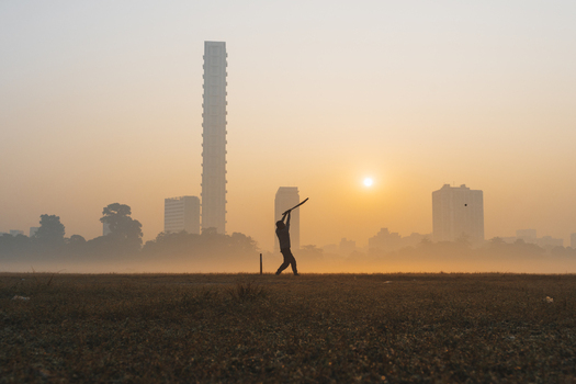 View of a lone cricketer silhouetted against the hazy dawn with Kolkata s skyline piercing the golden mist a tranquil moment frozen in time Kolkata West Bengal India. View of a lone cricketer silhouetted against the hazy dawn with Kolkata s skyline piercing the golden mist a tranquil moment frozen in time Kolkata West Bengal India.