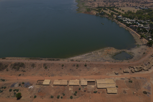 Aerial view of the Minjibir dam shoreline with small thatched structures and arid vegetation under a clear sky in Kano City Kano State Nigeria. Aerial view of the Minjibir dam shoreline with small thatched structures and arid vegetation under a clear sky in Kano City Kano State Nigeria.