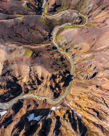 Aerial view of a winding river flowing through rugged volcanic terrain with patches of moss and snow in Iceland. Aerial view of a winding river flowing through rugged volcanic terrain with patches of moss and snow in Iceland.