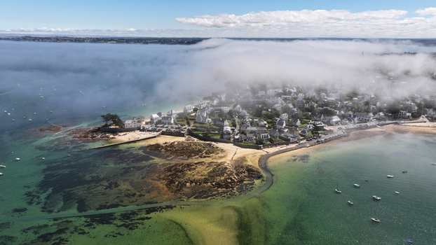 Aerial view of the fog laden coastline meeting quaint homes and the sandy beach shrouded in mist Carantec Bretagne France.
