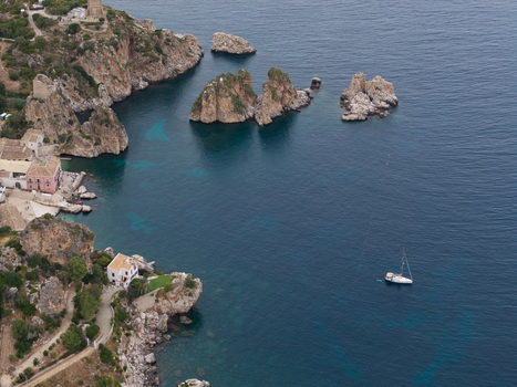 Aerial view of the Tonnara di Scopello with rocky cliffs turquoise sea and a sailboat anchored near the coast in Palermo Sicily Italy. Aerial view of the Tonnara di Scopello with rocky cliffs turquoise sea and a sailboat anchored near the coast in Palermo Sicily Italy.