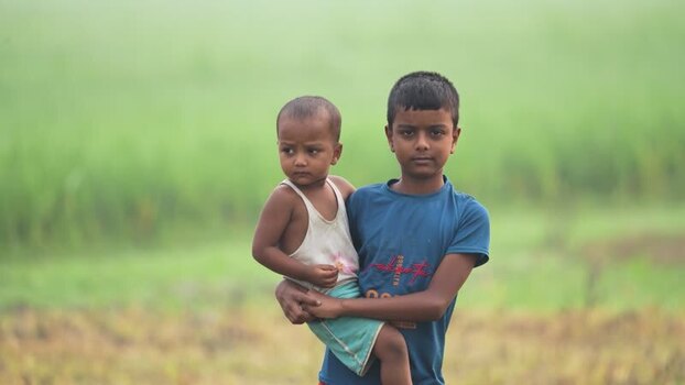 View of a boy carrying his younger brother in a field Bangladesh.
