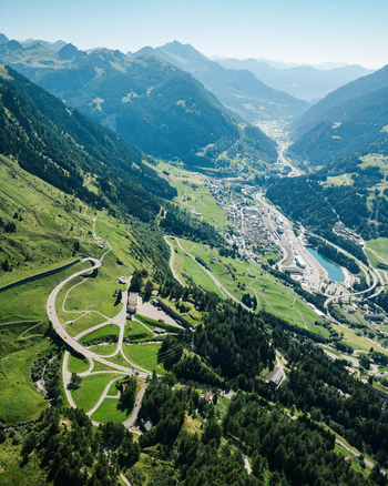 Aerial view of the winding mountain roads of the Furka Pass snaking through lush green slopes and pine forests towards the valley floor in Obergoms Valais Switzerland.