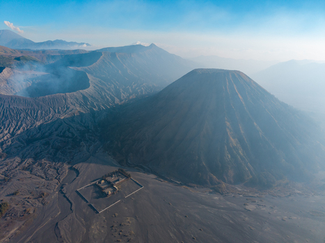 Aerial view of the volcanic landscape of Mount Bromo with its iconic cone smoking crater and a small temple in the vast sandy caldera in Tosari East Java Indonesia.