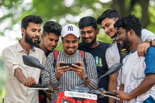 Bogura Bangladesh 26 October 2022 View of a group of young men gathered around a motorcycle smiling while looking at a smartphone screen together in an outdoor setting.