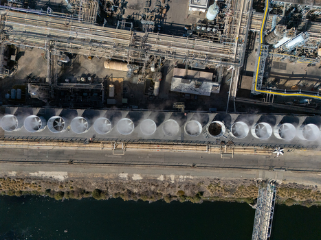 Aerial view of an industrial refinery complex with a row of large cooling towers emitting steam and complex piping infrastructure in Carson California United States.