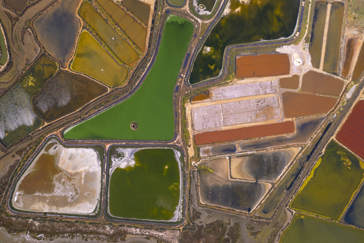 Aerial view of Salinas do Grelha featuring colorful salt evaporation ponds with shades of green brown and white reflecting the salt production process in Olhao Faro Portugal. Aerial view of Salinas do Grelha featuring colorful salt evaporation ponds with shades of green brown and white reflecting the salt production process in Olhao Faro Portugal.