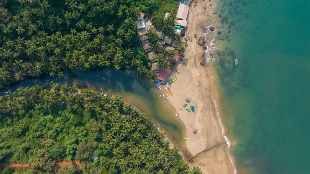 Aerial view of Cola Beach featuring a tranquil lagoon meeting the Arabian Sea surrounded by dense palm groves and colorful kayaks on the sandy shore Kola Goa India. Aerial view of Cola Beach featuring a tranquil lagoon meeting the Arabian Sea surrounded by dense palm groves and colorful kayaks on the sandy shore Kola Goa India.