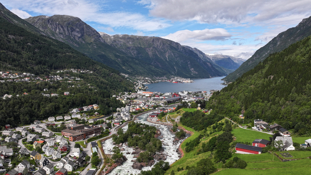 Aerial view of the town of Odda nestled in a deep valley between steep mountains with a rushing river flowing through the center towards the fjord in Odda Vestland Norway. Aerial view of the town of Odda nestled in a deep valley between steep mountains with a rushing river flowing through the center towards the fjord in Odda Vestland Norway.