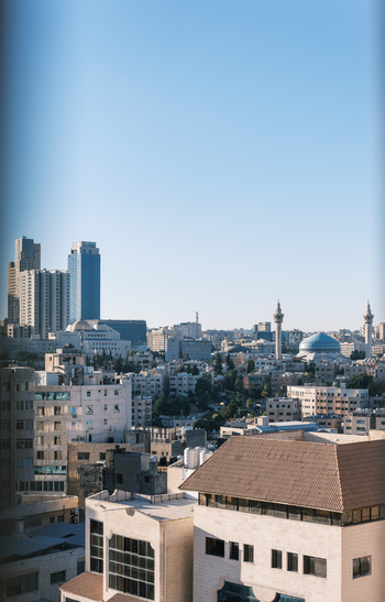 View of the Amman city skyline featuring the blue dome and minarets of the King Abdullah I Mosque surrounded by urban buildings and residential rooftops in Amman Amman Governorate Jordan.