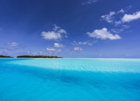 View of the turquoise lagoon surrounding One Foot Island in Aitutaki with lush palm trees and clear blue sky in Arutanga Cook Islands. View of the turquoise lagoon surrounding One Foot Island in Aitutaki with lush palm trees and clear blue sky in Arutanga Cook Islands.