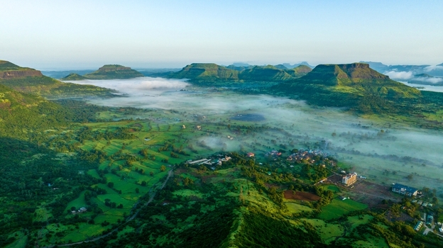 Aerial view of the lush green hills and valleys of Igatpuri with morning mist rolling over the landscape and small village settlements in Igatpuri Maharashtra India.