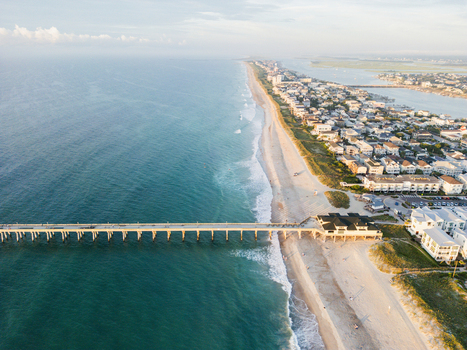 Aerial view of Johnnie Mercers Fishing Pier extending into the Atlantic Ocean with sandy beaches and coastal houses in Wrightsville Beach North Carolina United States. Aerial view of Johnnie Mercers Fishing Pier extending into the Atlantic Ocean with sandy beaches and coastal houses in Wrightsville Beach North Carolina United States.