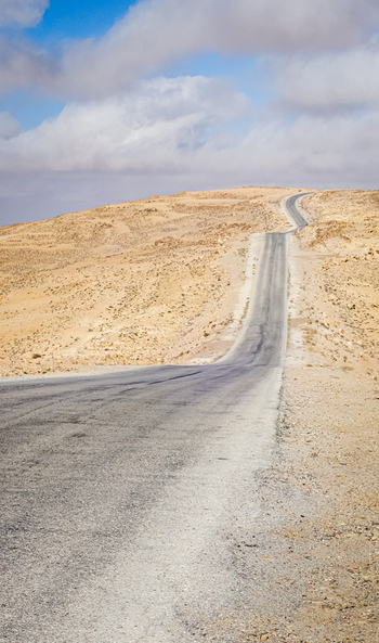 View of a paved road stretching through the vast arid landscape of the Wadi Rum Desert under a blue sky with scattered clouds in Wadi Rum Village Aqaba Governorate Jordan. View of a paved road stretching through the vast arid landscape of the Wadi Rum Desert under a blue sky with scattered clouds in Wadi Rum Village Aqaba Governorate Jordan.