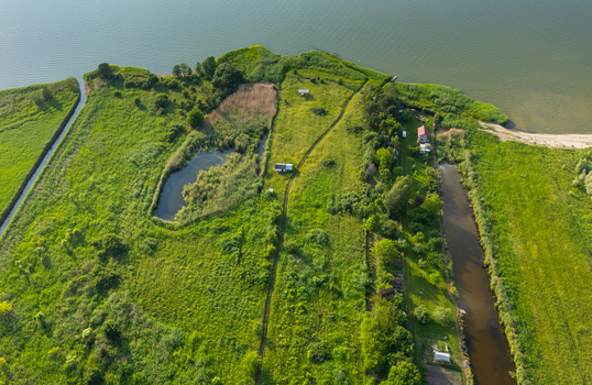 Aerial view of Vistula Lagoon with lush green fields small ponds and a canal flowing through the landscape in Tolkmicko Warmian Masurian Voiv Poland. Aerial view of Vistula Lagoon with lush green fields small ponds and a canal flowing through the landscape in Tolkmicko Warmian Masurian Voiv Poland.