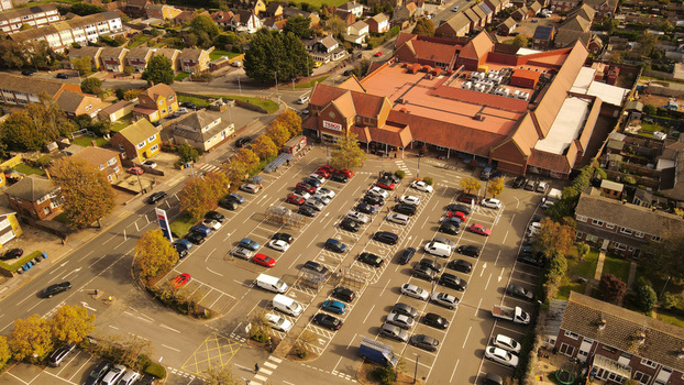 Aerial view of a Tesco supermarket with a large parking lot filled with cars surrounded by residential houses and autumn trees in England United Kingdom. Aerial view of a Tesco supermarket with a large parking lot filled with cars surrounded by residential houses and autumn trees in England United Kingdom.