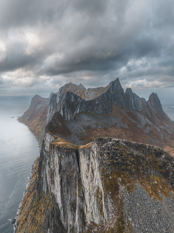 Aerial view of the dramatic jagged mountain peaks of Senja rising above the dark sea under a cloudy sky in Senja Troms Norway.