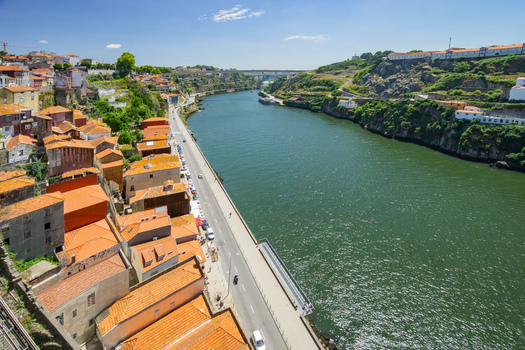 Aerial view of terracotta rooftops cascade down to the Douro River reflecting the clear sky above contrasting with the lush green hills Porto Porto District Portugal. Aerial view of terracotta rooftops cascade down to the Douro River reflecting the clear sky above contrasting with the lush green hills Porto Porto District Portugal.
