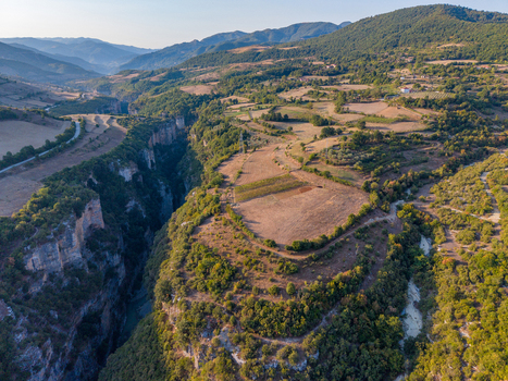 Aerial view of Osumi canyon featuring a deep river gorge surrounded by lush hills agricultural fields and rocky cliffs in Dhores Berat County Albania.