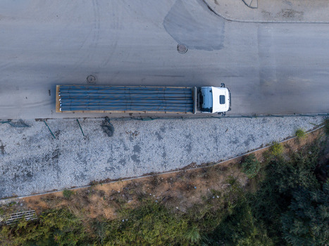 Aerial view of a white flatbed truck transporting a load of long metal pipes along a paved road next to a stone paved area and greenery in Istanbul Istanbul Turkiye. Aerial view of a white flatbed truck transporting a load of long metal pipes along a paved road next to a stone paved area and greenery in Istanbul Istanbul Turkiye.