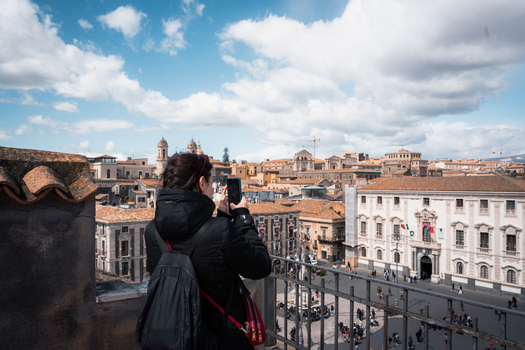 View of a woman capturing the warm hues of historic buildings and a bustling square under a bright airy sky Taormina Sicily Italy. View of a woman capturing the warm hues of historic buildings and a bustling square under a bright airy sky Taormina Sicily Italy.