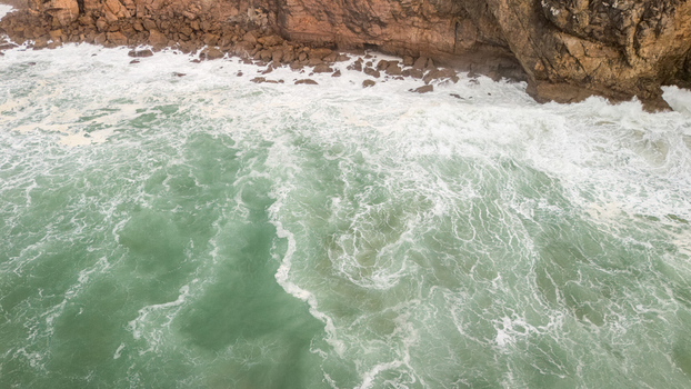 Aerial view of rough turquoise sea waves crashing against the rugged limestone cliffs with white foam in Sagres Faro Portugal. Aerial view of rough turquoise sea waves crashing against the rugged limestone cliffs with white foam in Sagres Faro Portugal.