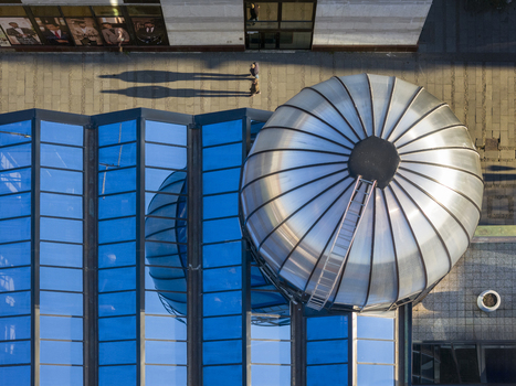 Aerial view of a modern building with a metallic dome and blue glass roof with people walking on the sidewalk casting long shadows in Belgrade City of Belgrade Serbia. Aerial view of a modern building with a metallic dome and blue glass roof with people walking on the sidewalk casting long shadows in Belgrade City of Belgrade Serbia.