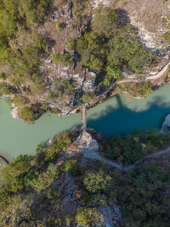 Aerial view of Osumi Canyon with a narrow pedestrian bridge crossing the turquoise river between steep rocky cliffs and dense forest in Dhores Berat County Albania.