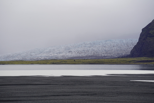 View of Skaftafell glacier with its rugged ice formations mossy green foreground and dark volcanic sand under a cloudy sky in Skaftafell Sveitarfelagid Hornaf Iceland. View of Skaftafell glacier with its rugged ice formations mossy green foreground and dark volcanic sand under a cloudy sky in Skaftafell Sveitarfelagid Hornaf Iceland.