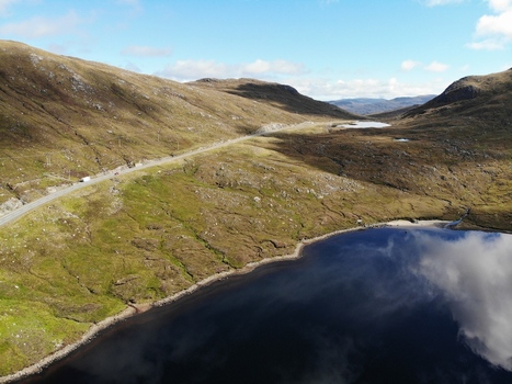Aerial view of a winding road passing through rugged hillsides next to a dark lake reflecting the sky in Huisinis Scotland United Kingdom.