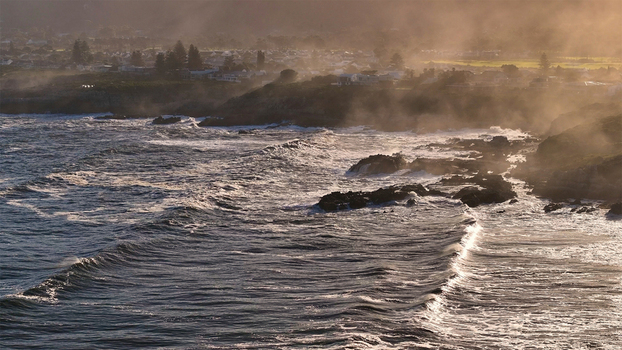 Aerial view of the rugged coastline with crashing waves and sea spray under golden sunlight near a coastal town in Cape Town Western Cape South Africa. Aerial view of the rugged coastline with crashing waves and sea spray under golden sunlight near a coastal town in Cape Town Western Cape South Africa.