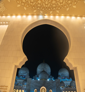 View of the Sheikh Zayed Grand Mosque domes illuminated at night through a decorative archway with intricate ceiling patterns in Abu Dhabi Abu Dhabi United Arab Emirates. View of the Sheikh Zayed Grand Mosque domes illuminated at night through a decorative archway with intricate ceiling patterns in Abu Dhabi Abu Dhabi United Arab Emirates.