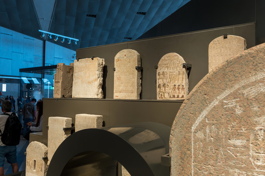Giza Egypt 16 May 2026 View of ancient stone stelae and artifacts on display inside the modern Grand Egyptian Museum with visitors in the background.