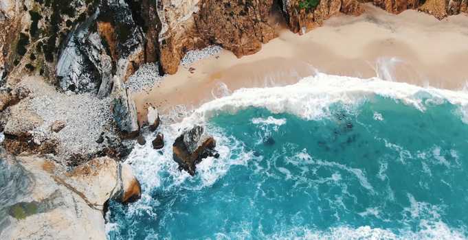 Aerial view of Praia da Ursa climbing area with rugged cliffs turquoise ocean waves crashing against the sandy shore and rocky formations in Colares Lisbon Portugal. Aerial view of Praia da Ursa climbing area with rugged cliffs turquoise ocean waves crashing against the sandy shore and rocky formations in Colares Lisbon Portugal.