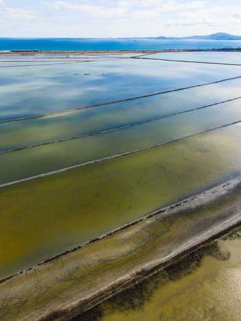 Aerial view of the geometric salt evaporation ponds at Lake Atanasovsko with the Black Sea coast and distant hills under a bright sky in Burgas Burgas Bulgaria. Aerial view of the geometric salt evaporation ponds at Lake Atanasovsko with the Black Sea coast and distant hills under a bright sky in Burgas Burgas Bulgaria.