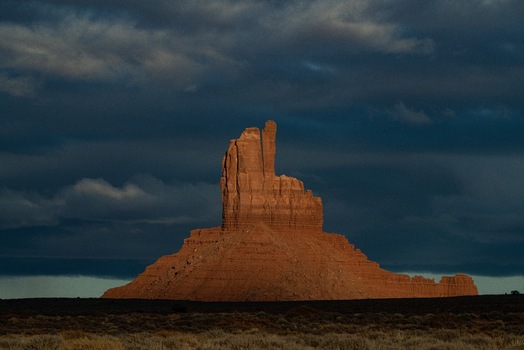 View of the sandstone butte in Monument Valley Tribal Park illuminated by golden hour light against dramatic dark storm clouds in Oljato Monument Valley Utah United States.