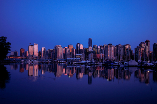 Aerial view of the Vancouver skyline at dusk with buildings reflected in the calm water of the harbor and sailboats moored in the foreground in Vancouver British Columbia Canada.