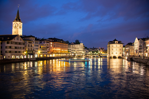 View of the Limmat River at dusk with the historic St. Peter Church tower illuminated buildings and reflections on the water in Zurich Zurich Switzerland.