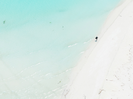 Aerial view of a lone figure on brilliant white sand where vivid turquoise waters gently lap Thuraakunu Thiladhunmathee Uthuruburi Maldives. Aerial view of a lone figure on brilliant white sand where vivid turquoise waters gently lap Thuraakunu Thiladhunmathee Uthuruburi Maldives.