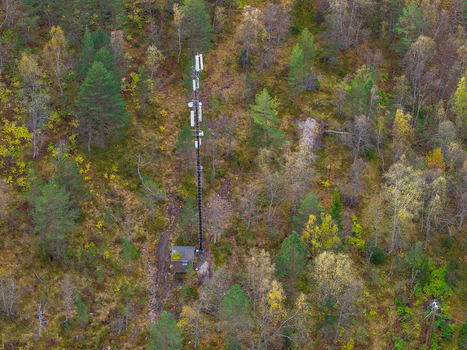 Aerial view of a tall telecommunications cell tower situated in a dense forest with autumn foliage in Fjord More og Romsdal Norway.