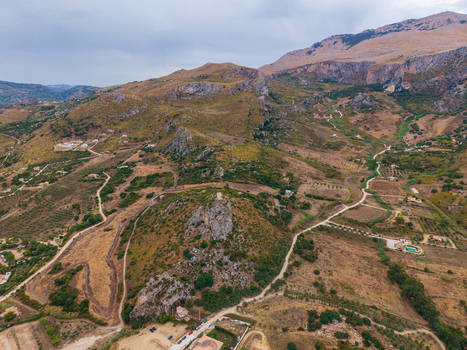 Aerial view of the rugged mountainous landscape near Palermo featuring rocky hills winding dirt paths and scattered rural vegetation under a cloudy sky in Palermo Sicily Italy. Aerial view of the rugged mountainous landscape near Palermo featuring rocky hills winding dirt paths and scattered rural vegetation under a cloudy sky in Palermo Sicily Italy.