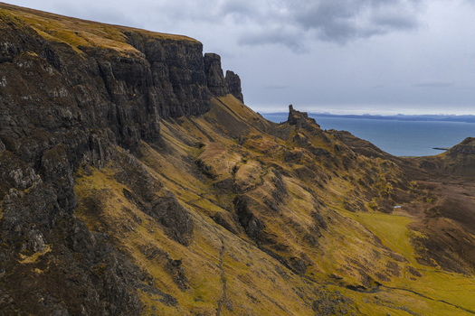 Aerial view of the dramatic basalt cliffs and grassy slopes of The Quiraing overlooking the sea under a cloudy sky at Isle of Skye Scotland United Kingdom. Aerial view of the dramatic basalt cliffs and grassy slopes of The Quiraing overlooking the sea under a cloudy sky at Isle of Skye Scotland United Kingdom.