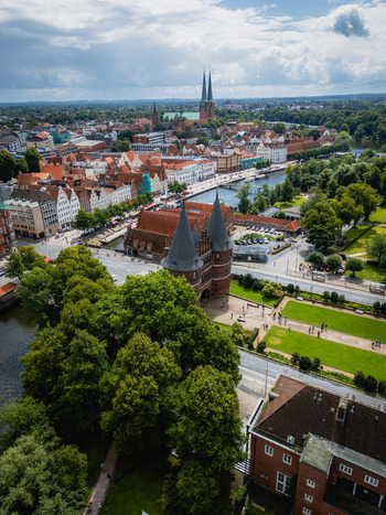 Aerial view of the Holsten Gate framed by vibrant green trees with the old town s red rooftops and the twin spires of L&uuml;beck Cathedral in the distance L&uuml;beck Schleswig Holstein Germany.