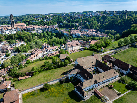 Aerial view of Monastere de Montorge surrounded by green meadows with the historic skyline of Fribourg and St. Nicholas Cathedral in the background Fribourg Fribourg Switzerland.