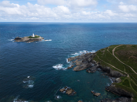 Aerial view of Godrevy Lighthouse on a rocky island surrounded by the blue ocean and green cliffs with coastal paths in Gwithian England United Kingdom. Aerial view of Godrevy Lighthouse on a rocky island surrounded by the blue ocean and green cliffs with coastal paths in Gwithian England United Kingdom.