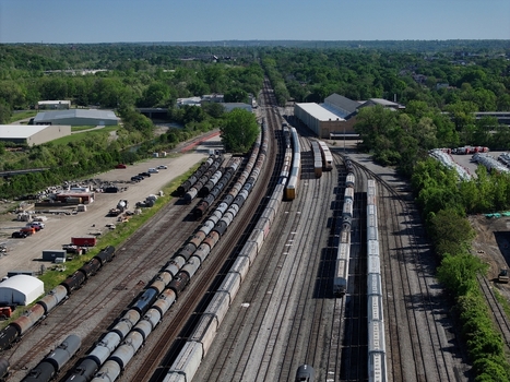 Aerial view of freight trains parked on multiple tracks in a railway yard surrounded by lush green trees and industrial buildings Cincinnati OH United States. Aerial view of freight trains parked on multiple tracks in a railway yard surrounded by lush green trees and industrial buildings Cincinnati OH United States.