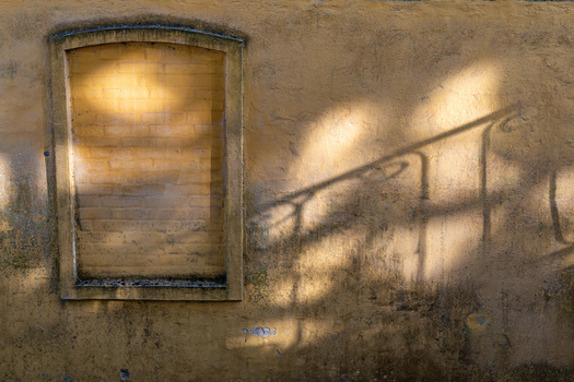View of a weathered yellow brick wall with a bricked up window niche and shadows of a railing in Ribe Denmark. View of a weathered yellow brick wall with a bricked up window niche and shadows of a railing in Ribe Denmark.